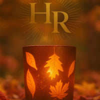 Decorative candle with leaf patterns and HarleyRae initials on a blurred autumn background