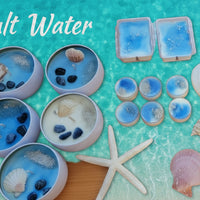 A collection of blue wax melts with varying sizes, displayed alongside seashells and a starfish on a wooden surface. Some melts are in cylindrical containers, while others are freestanding.