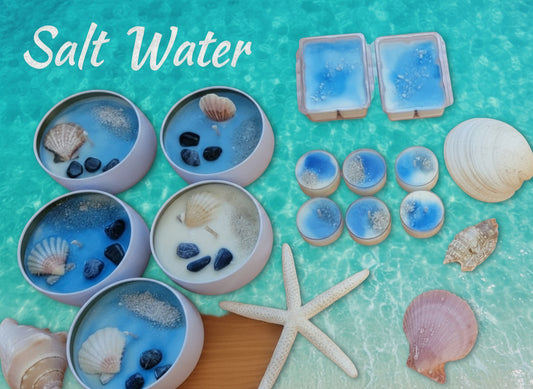 A collection of blue wax melts with varying sizes, displayed alongside seashells and a starfish on a wooden surface. Some melts are in cylindrical containers, while others are freestanding.